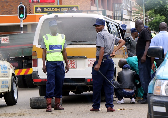 Traffic police stand guard while a kombi crew changes a punctured tyre at the intersection of Herbert Chitepo Street and 9th Avenue in Bulawayo. Traffic police threw spikes under the moving kombi which was carrying passengers