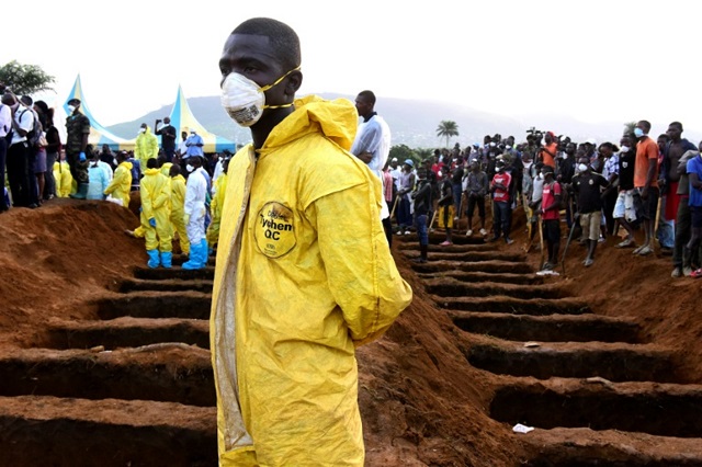 Men wait beside empty graves for the coffins of mudslide victims at Waterloo cemetery, near Freetown | © AFP | SEYLLOU