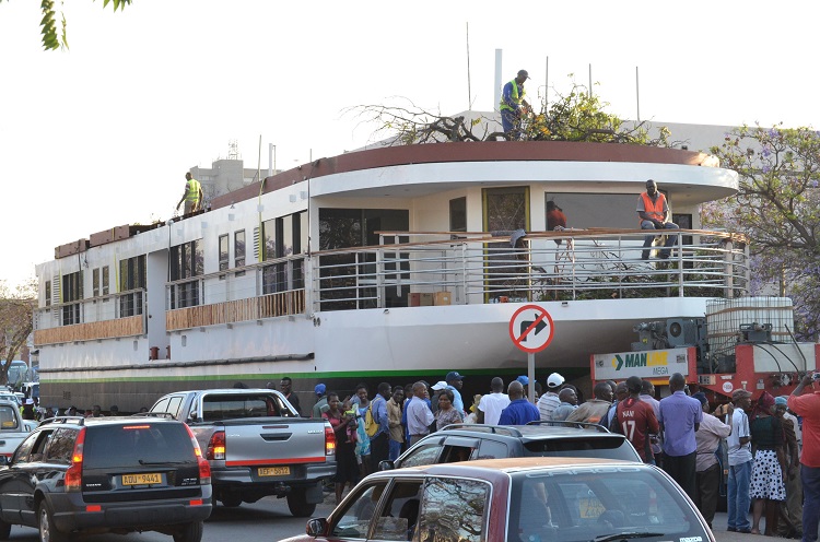 Crew members transporting the houseboat are seen cutting trees along the road to enable the trucking touring it to maneuver past